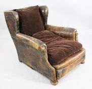 A distressed leather wingback armchair, with deep seat and brass studs, on bun feet