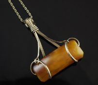 A gold mounted amber pendant, the curved rectangular piece of amber set in an open scroll mount, on