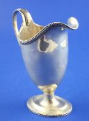A Victorian silver helmet shaped pedestal cream jug, with engraved armorial and beaded handle and
