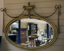 An Adam style oval gilt wall mirror, with urn and ribbon swag crest and bevelled plate glass,
