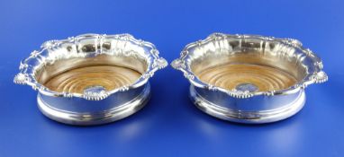 A pair of William IV silver wine coasters, with shell and scroll borders and turned wooden bases