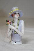 A 1920`s Continental porcelain pin cushion doll, with head and torso, holding flowers in her right