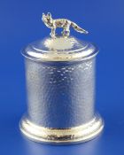 An Edwardian hammered silver tobacco jar and cover, of cylindrical form, with fox finial and gilt