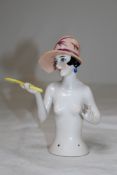 A 1920`s Continental porcelain pin cushion doll, with head and torso, holding a hand mirror,