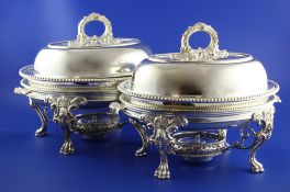 An ornate pair of silver plated entree dishes on two handled warming dishes and stands with