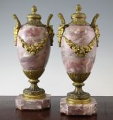 A pair of late 19th century ormolu and pink marble pedestal urns, with stiff leaf and reeded lids,