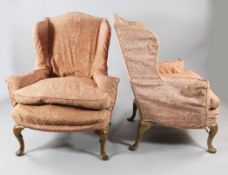 A pair of George I style wingback armchairs, with pink patterned loose covers, on carved cabriole