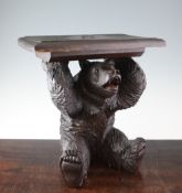 An early 20th century Black Forest carved model of a seated bear, holding aloft a square carved