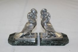 A pair of silvered metal cockatiels bookends, on veined black/green marble base, signed Frecourt,