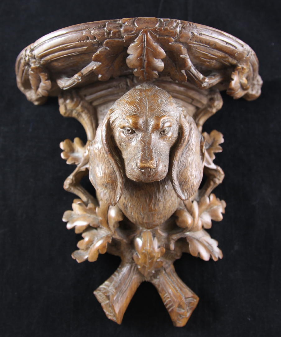 A late 19th century Black Forest carved wall bracket, decorated with a dog`s head, oak leaves and