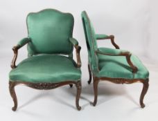 A pair of French Louis XV style carved walnut fauteuils, upholstered in a brass studded green