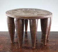 A West African circular hardwood Nupe stool, the top with carved sunburst motif and ten tapering