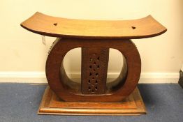 A carved African hardwood Ashanti stool, of typical form, with shaped top and rectangular plinth