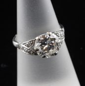 A platinum and solitaire diamond ring with diamond set foliate shoulders and central stone