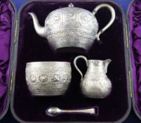 A cased Victorian silver three piece tea set with sugar tongs, of circular form, embossed with signs