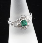 An 18ct white gold, emerald and diamond cluster ring, of flowerhead design with diamond set split