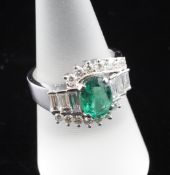 An 18ct white gold, emerald and diamond fancy cluster ring, the central oval cut emerald weighing