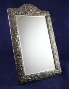 A late Victorian repousse silver easel mirror, of domed rectangular form, decorated with foliate