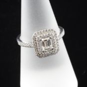 A white gold and diamond cluster ring, of square form, the central emerald cut stone weighing 0.