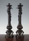 A pair of Japanese bronze candlesticks, c.1900, the columns cast in low relief with scrolls and
