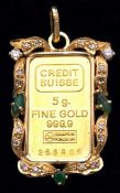 A 5gr. pure gold (999.9) ingot encased in a gold pendant frame set with three emeralds and 18