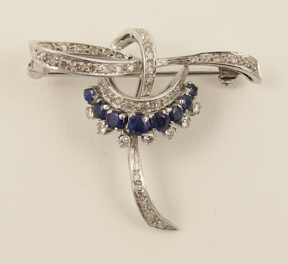 A sapphire and diamond brooch in unhallmarked white metal in a swirl design pave set with diamonds