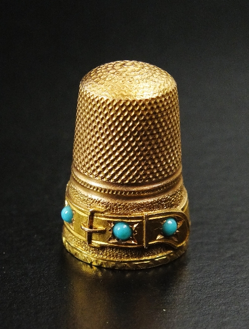 A yellow metal thimble, of typical honeycomb design with decorative buckle rim set with three