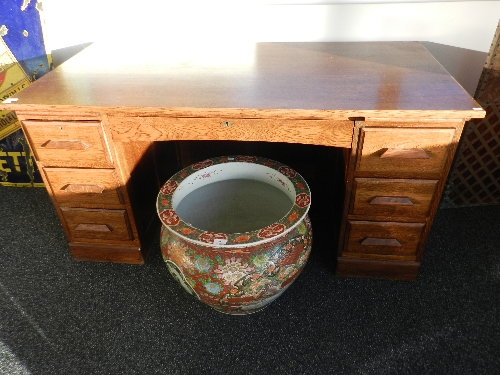 An oak pedestal desk with central drawer flanked by two slides and six drawers on plinth base