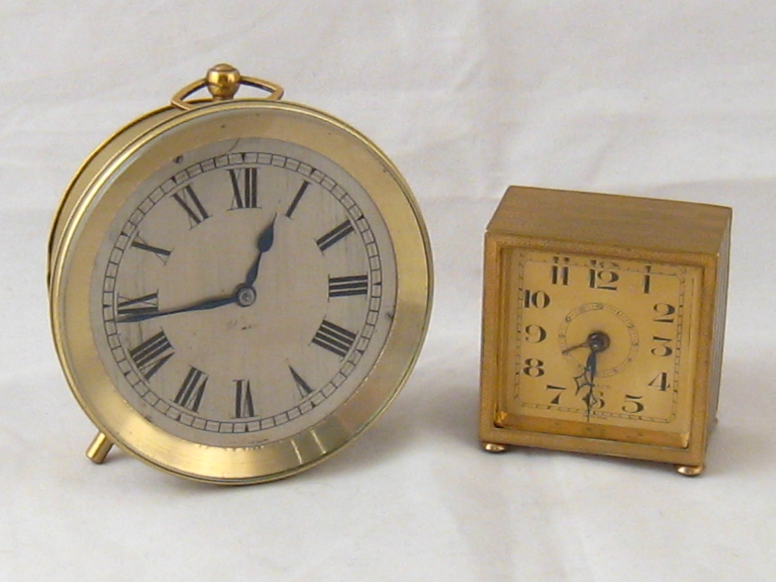 A circular bedside clock with key wind, 10cm. diameter, and an alarm clock, 6 cms square, both in