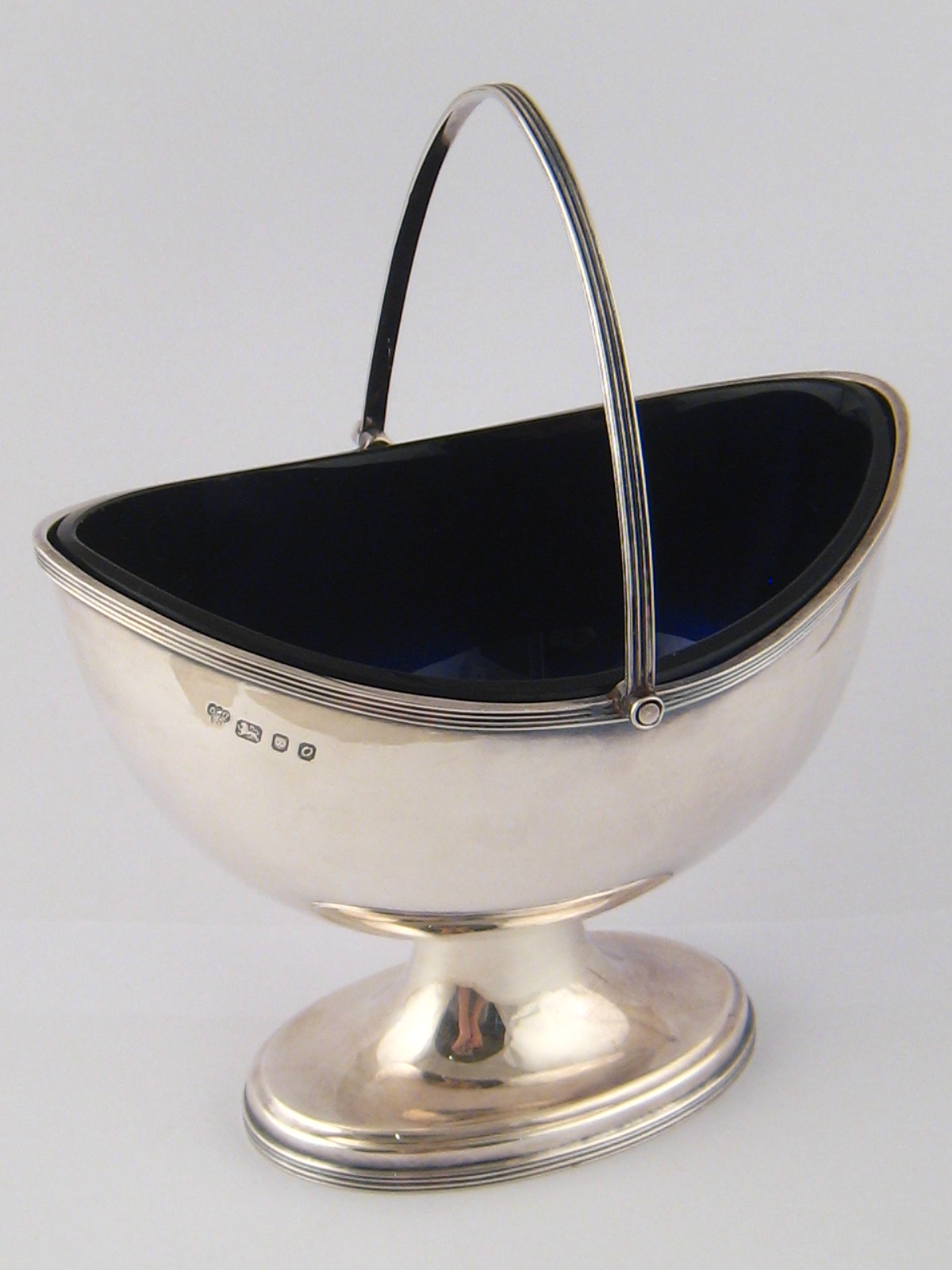 A deep oval navette shaped silver sucrier on spread foot with ribbed rim, swing handle and blue