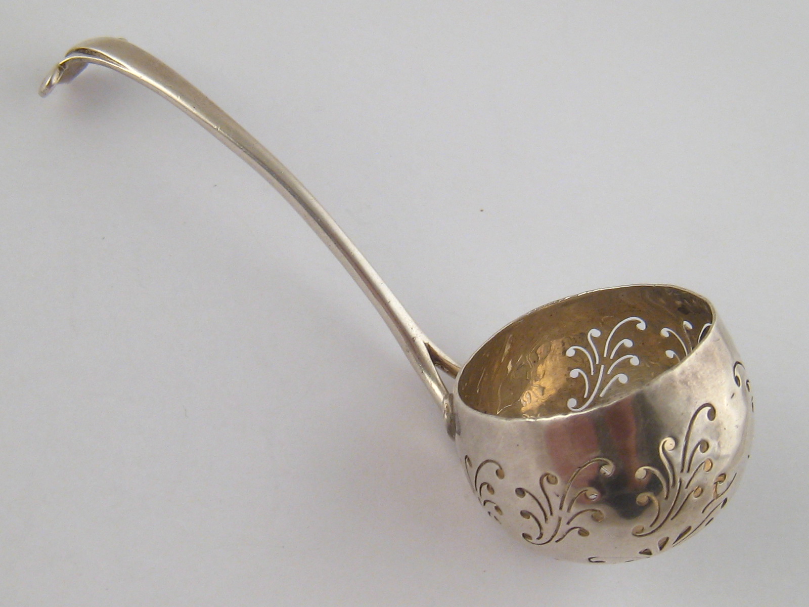 A silver sifter ladle, the deep bowl with scrolling piercing, the bifurcated handle in the Art