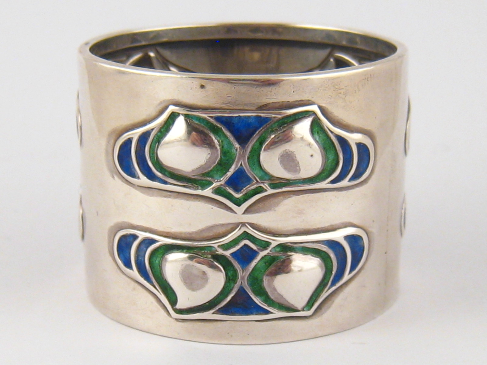 A Liberty &Co. Arts and Crafts silver napkin ring with three pairs of embossed enamel panels,
