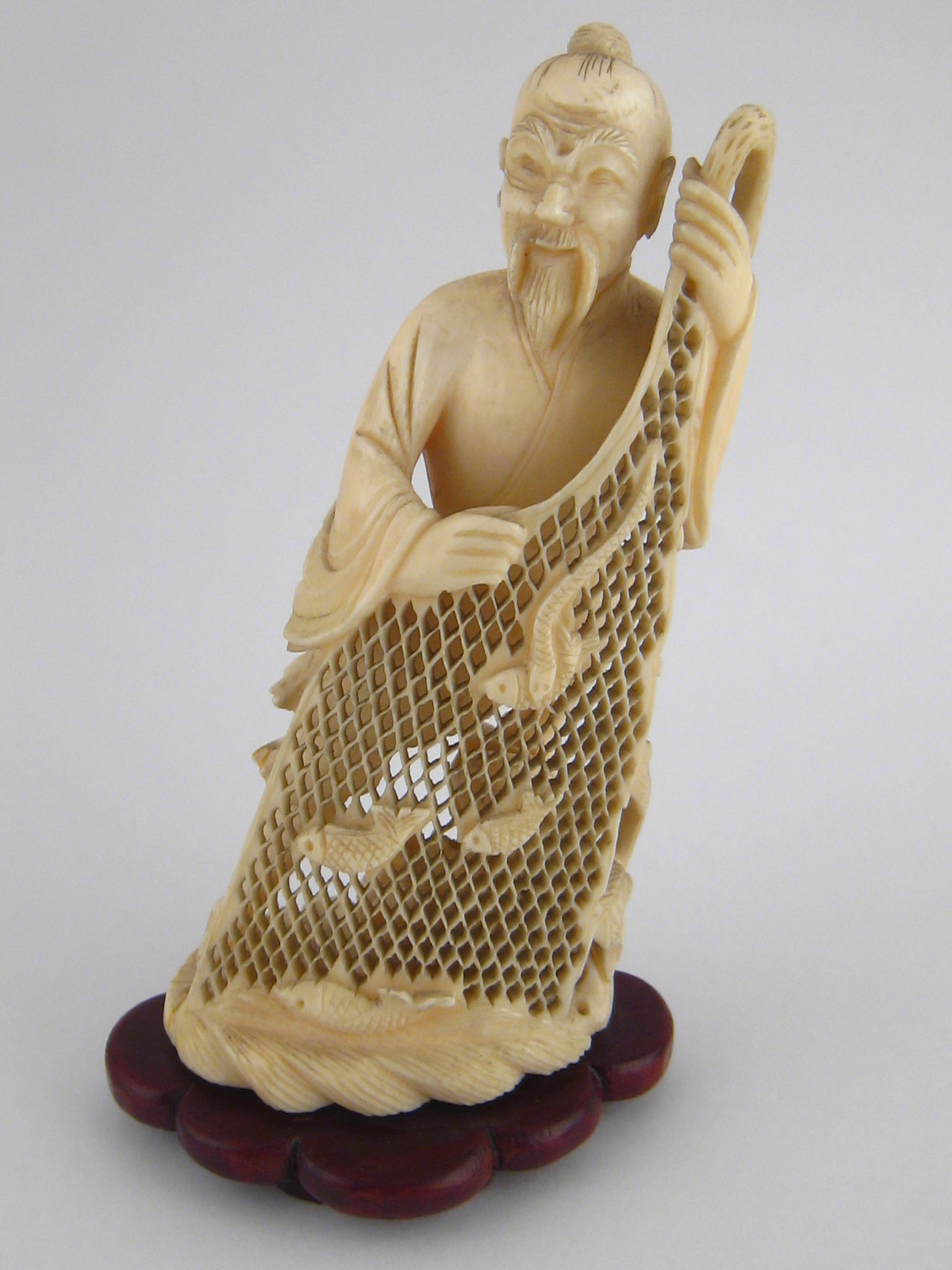 A Japanese ivory figure of a fisherman displaying his net with fish, c. 1930, ht. 13cm, on