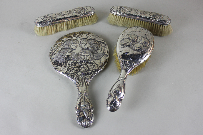 Four pieces of silver back dressing table items, each embossed with cherubs, comprising hand