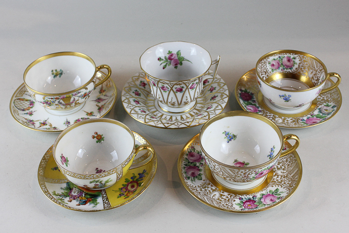 Five various Dresden porcelain cups and saucers decorated with flowers and enriched with gilt,