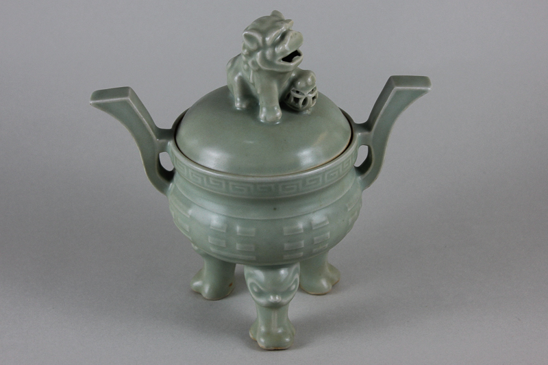 A pale green glazed Chinese porcelain koro with temple dog finial on three mask supports, 22cm high