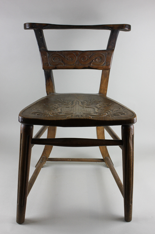 An early 20th century chair with carved wooden seat, dated 1915 and scorched burnt back, cut down