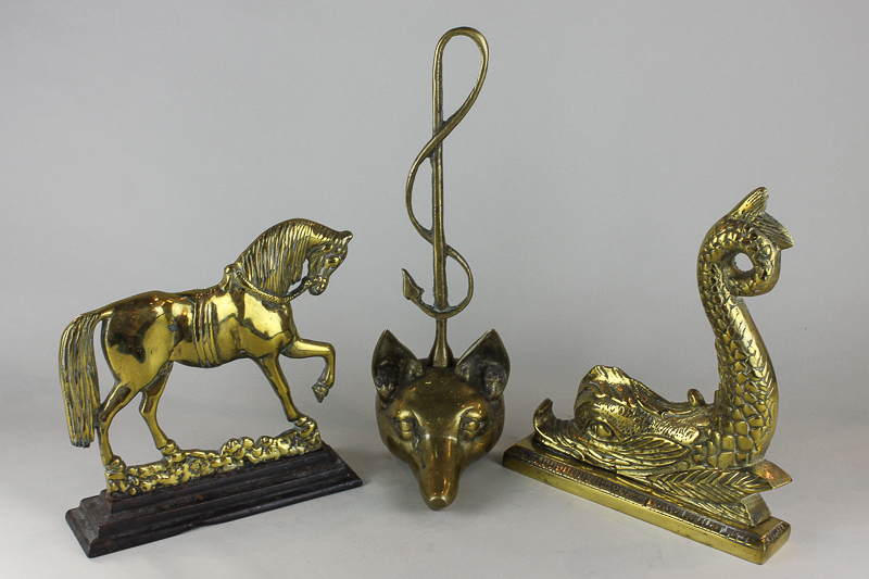 A brass and iron horse door stop, another of a brass dolphin and another of a fox head