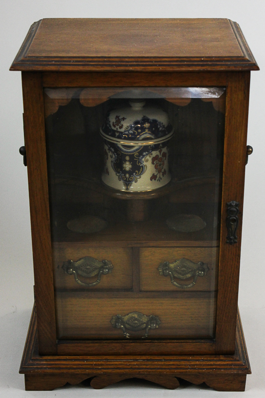 An early 20th century oak smoker`s cabinet with tobacco pot and three small drawers enclosed by one