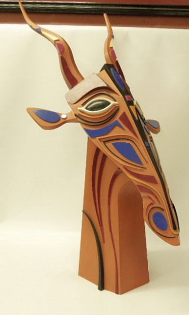 A CONTEMPORARY WOOD FORM SCULPTURE OF A GIRAFFE HEAD PAINTED AND DECORATED WITH APPLIED COLOURED