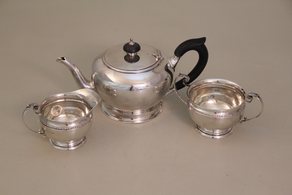 A silver cream jug and sugar basin, with tongue and dart border and leaf capped scroll handle, on