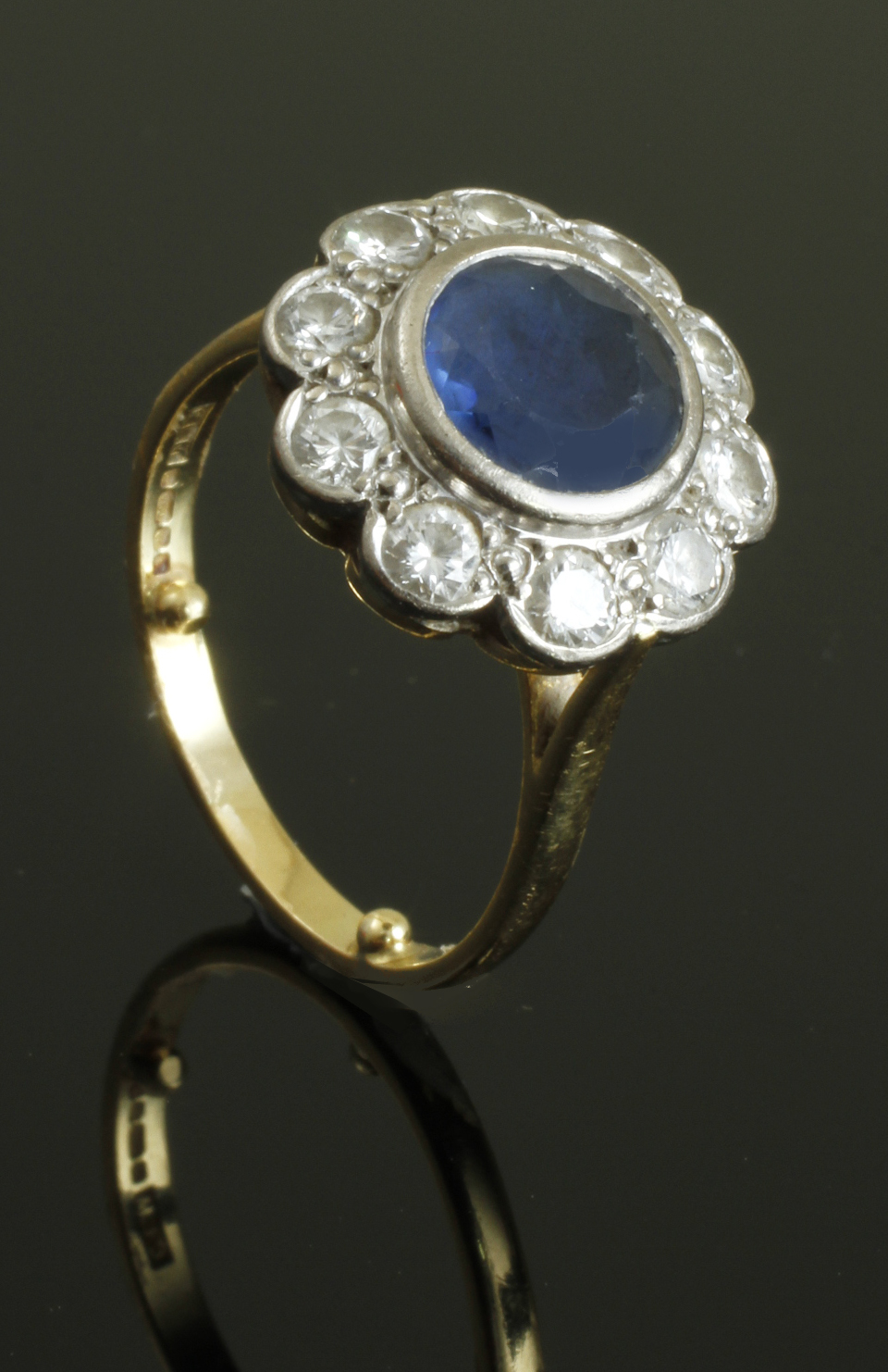 A sapphire and diamond cluster ring, the circular cut sapphire in rub over mount within a border of