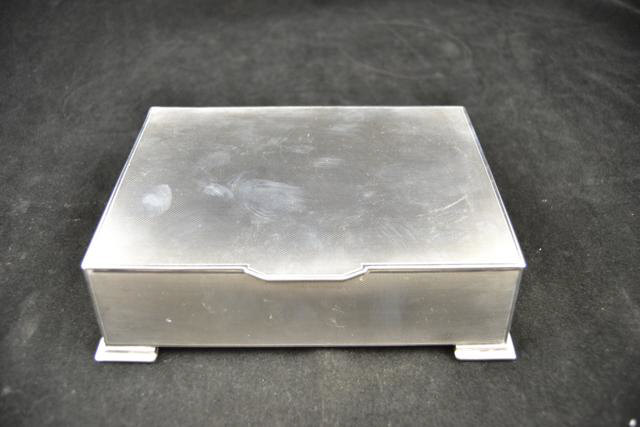 An engine turned Art Deco style cigarette box with inscription to underside of lid, 17cm wide,