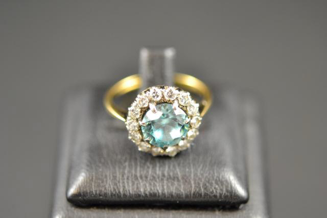 An 18ct gold and platinum ring mounted with centre blue stone surrounded by fourteen diamonds,