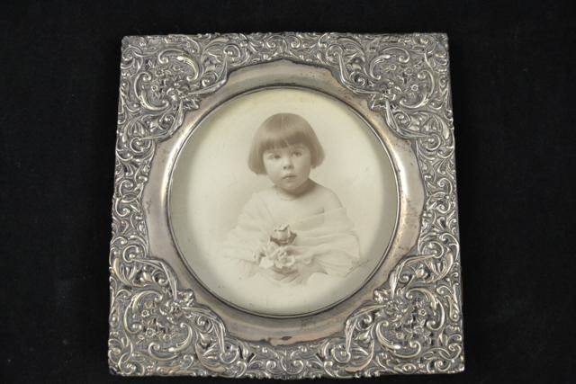 A silver photo frame embossed with scroll and foliate decoration, circular recess for photo,