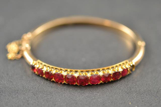 A 9ct gold bangle set with ten rubies, safety chain - approx gross weight 11.6g