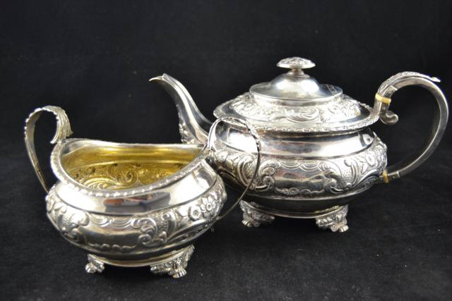 A George IV embossed silver circular teapot decorated with leaves and flowers, four paw feet,