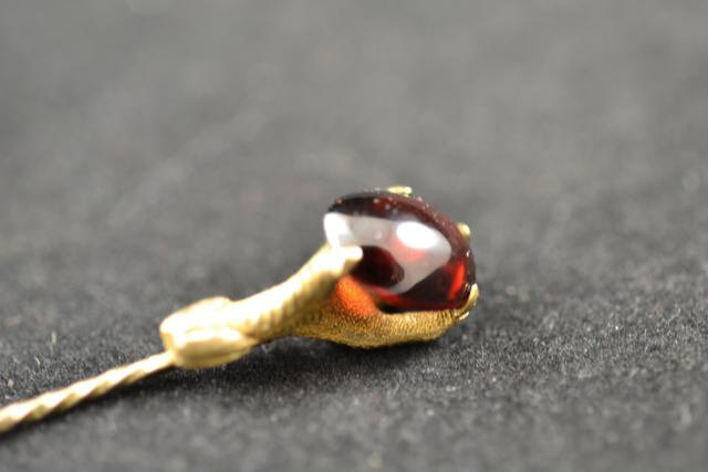 An unmarked yellow metal stick pin in the shape of a claw holding a garnet