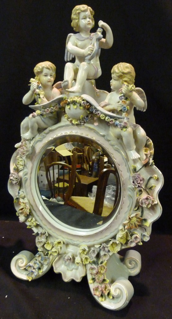 A Porcelain Table Mirror with Putti Surmount, raised upon scroll legs and with foliate encrusted