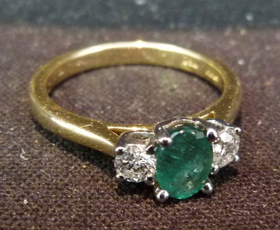 An 18ct. Yellow Gold Emerald and Diamond Ring, with an oval emerald flanked by diamonds within a